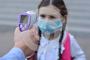 Temperature check in school . Child in medical mask in class in covid-19 outbreak.Teacher with thermometer at preschool or school