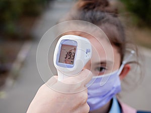 Temperature measurement of a sick child with a non-contact digital infrared thermometer showing fever. Schoolgirl girl