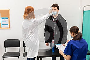 Temperature measurement of a young man in the entrance of a clinic performed by medical staff in the face of a pandemic