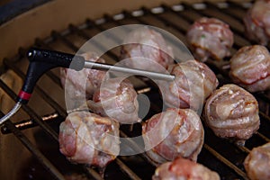 Temperature probe measuring inside temp from meatballs with bacon on BBQ