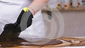 Tempering melted chocolate on natural stone. Woman`s hands and spatula close-up.