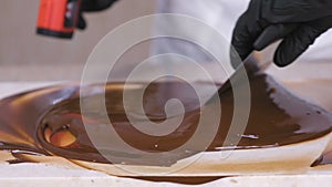 Tempering melted chocolate on natural stone. Woman`s hands and spatula close-up.