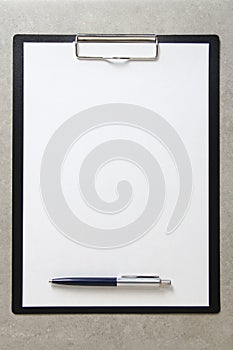 Template of white paper with a ballpoint pen on light grey concrete background in a black tablet with a clip. Concept of