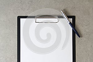 Template of white paper with a ballpoint pen on light grey concrete background in a black tablet with a clip. Concept of new idea