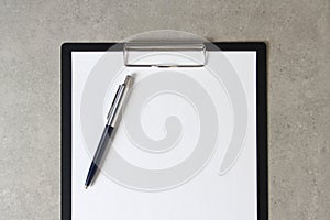 Template of white paper with a ballpoint pen on light grey concrete background in a black tablet with a clip. Concept of new idea