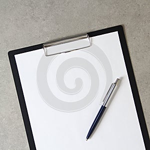 Template of white paper with a ballpoint pen on light grey concrete background in a black tablet with a clip. Concept of new idea