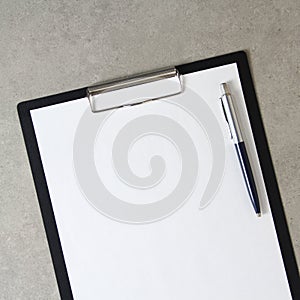 Template of white paper with a ballpoint pen on light grey concrete background in a black tablet with a clip. Concept of new idea