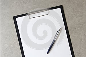 Template of white paper with a ballpoint pen on light grey concrete background in a black tablet with a clip. Concept of new idea