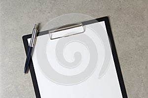 Template of white paper with a ballpoint pen on light grey concrete background in a black tablet with a clip. Concept of new idea