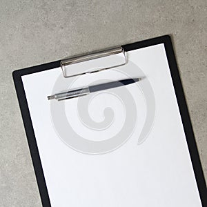 Template of white paper with a ballpoint pen on light grey concrete background in a black tablet with a clip. Concept of new idea