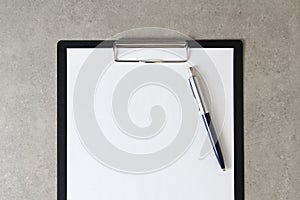 Template of white paper with a ballpoint pen on light grey concrete background in a black tablet with a clip. Concept of new idea