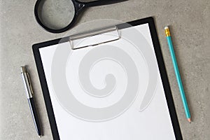 Template of white paper with a ballpoint pen, magnifying glass and simple pencil on light grey concrete background in a black