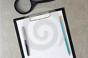 Template of white paper with a ballpoint pen, magnifying glass and simple pencil on light grey concrete background in a black