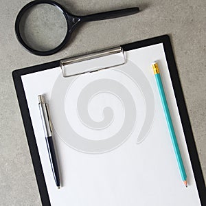 Template of white paper with a ballpoint pen, magnifying glass and simple pencil on light grey concrete background in a black