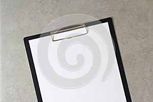 Template of white paper on light grey concrete background in a black tablet with a clip. Concept of new idea, business plan and