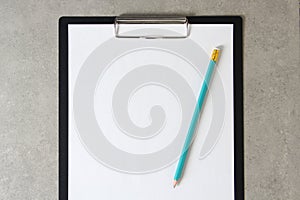 Template of white paper with simple pencil on light grey concrete background in a black tablet with a clip. Concept of new idea,
