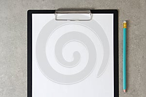 Template of white paper with simple pencil on light grey concrete background in a black tablet with a clip. Concept of new idea,