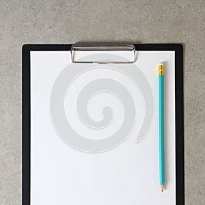 Template of white paper with simple pencil on light grey concrete background in a black tablet with a clip. Concept of new idea,