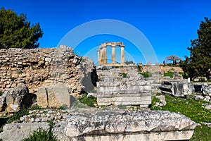 Temple of Apollo in ancient Corinth Greece viewed from down the hll in the excavated ruins with unidentifiable tourists taking pic