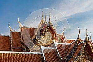 Temple Rooftop in Bangkok. Red tiles, golden decorations. Blue sky and clouds in background.