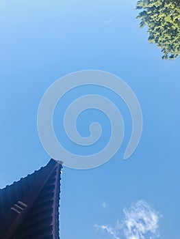 Temple`s eaves corner against tree, blue sky background.