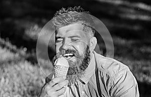 Temptation concept. Bearded man with ice cream cone. Man with beard and mustache on happy face enjoy ice cream, grass on