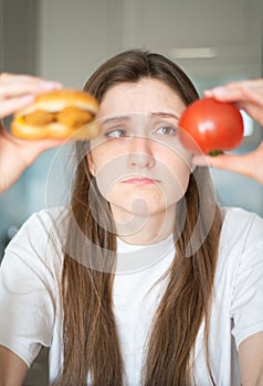 Temptation of junk food. The girl is thinking about what to eat. A beautiful woman holds a tomato and cheeseburger and