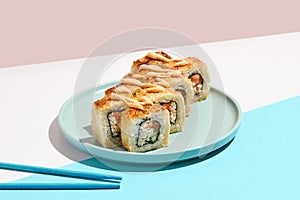 Tempura maki roll on ceramic plate with chopsticks. Hot sushi with salmon, crab and cucumber inside, spicy mayo topped. Modern