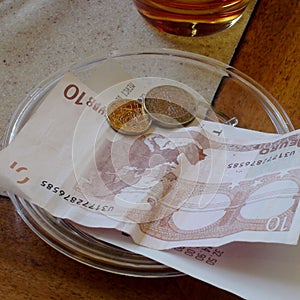 Ten Euro Bill with Coins on Plate on Wooden Table in Restaurant.
