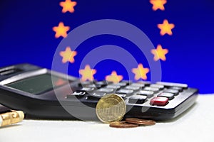 Ten Germany euro cent on obverse and two coin of two euro cent on white floor with black calculator and pencil, Euro flag.