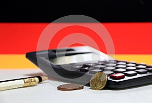 Ten Germany euro cent on reverse and two coin of two euro cent on white floor with black calculator and pencil, Germany flag.