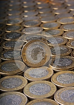 Ten Mexican pesos coin over more coins aligned and stacked