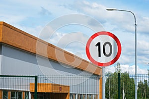 Ten miles or kilometers per hour speed limit sign against a clear sky and building.