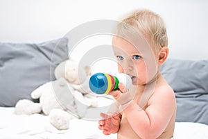 Ten month baby blond boy sitting on bed and playing with toy. Little kid in nappy portrait at home. Baby care concept,
