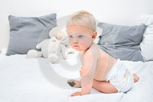 Ten month baby boy sitting on bed and looking back. Little kid in nappy at home. Little kid in nappy. Byby care concept,