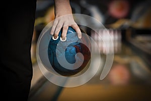 Ten pin bowling ball being held in hand close up, with bowling lane and pins background