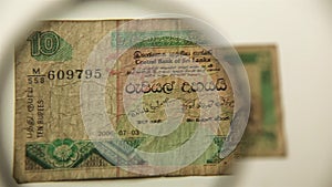 Ten Sri Lanka Rupees and magnifying glass.