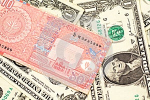 A ten taka note from Bangladesh on a background of dollar bills