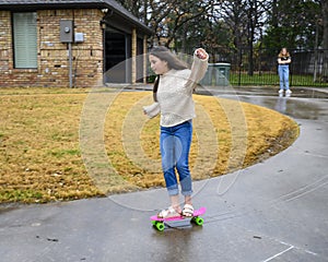 Ten year-old Amerasian girl skateboards down her driveway while her thirteen year old Caucasian cousin watches in Edmond, Oklahoma