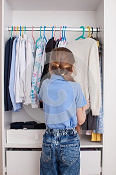 A ten-year-old girl chooses clothes in the closet.