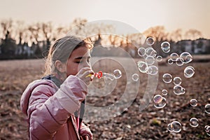 Ten years pretty girl blowing soap bubbles in the forest at sunset, warm walking in early spring