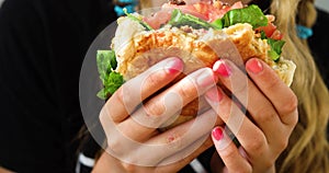 Tenager girl eats a hamburger with pork cutlet, lettuce, tomato, pickle in a cafe. Summer day