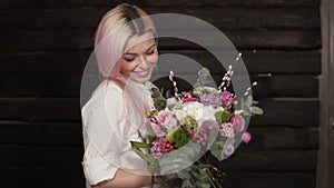 Tender, beautiful girl whirls with flowers in hands, enjoying the beauty of a bouquet. Dark background