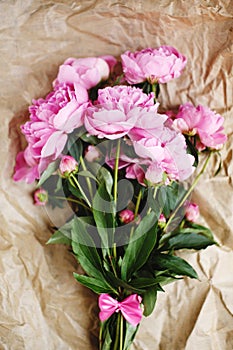 Tender bouquet of pink peonies flowers in sunlight on wrinkled craft paper background
