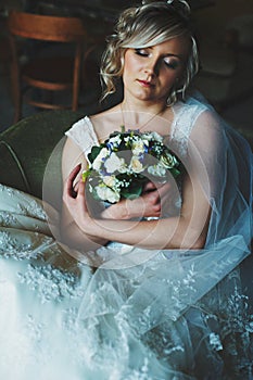 A tender bride wearing lace dress daydreams holding a bouquet in photo