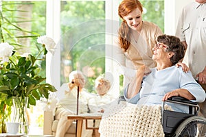 Tender caregiver saying goodbye to an elderly pensioner in a wheelchair in a day care facility. A companion pushing photo