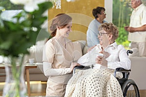 Tender caretaker making an elderly woman ia a wheelchair laugh i