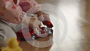 Tender childs hands playing with red car model and tiny teddy on wooden floor