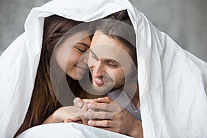 Tender couple relaxing under blanket on Sunday morning in bed