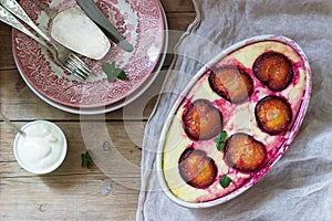 Tender curd casserole with plums and semolina, served with cinnamon and mint leaves on a wooden background